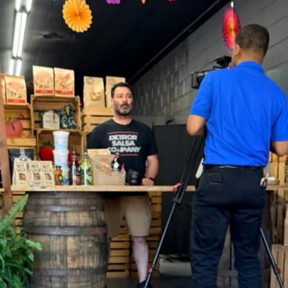 Ray Gomez behind the shop counter, being filmed by a Channel 7 camera operator.