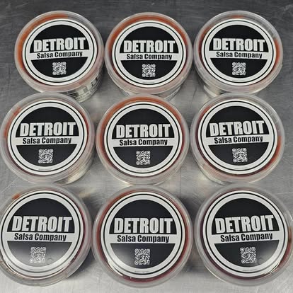 Nine Detroit Salsa Company tubs from above, each lid with the round black and white badge and a QR code.
